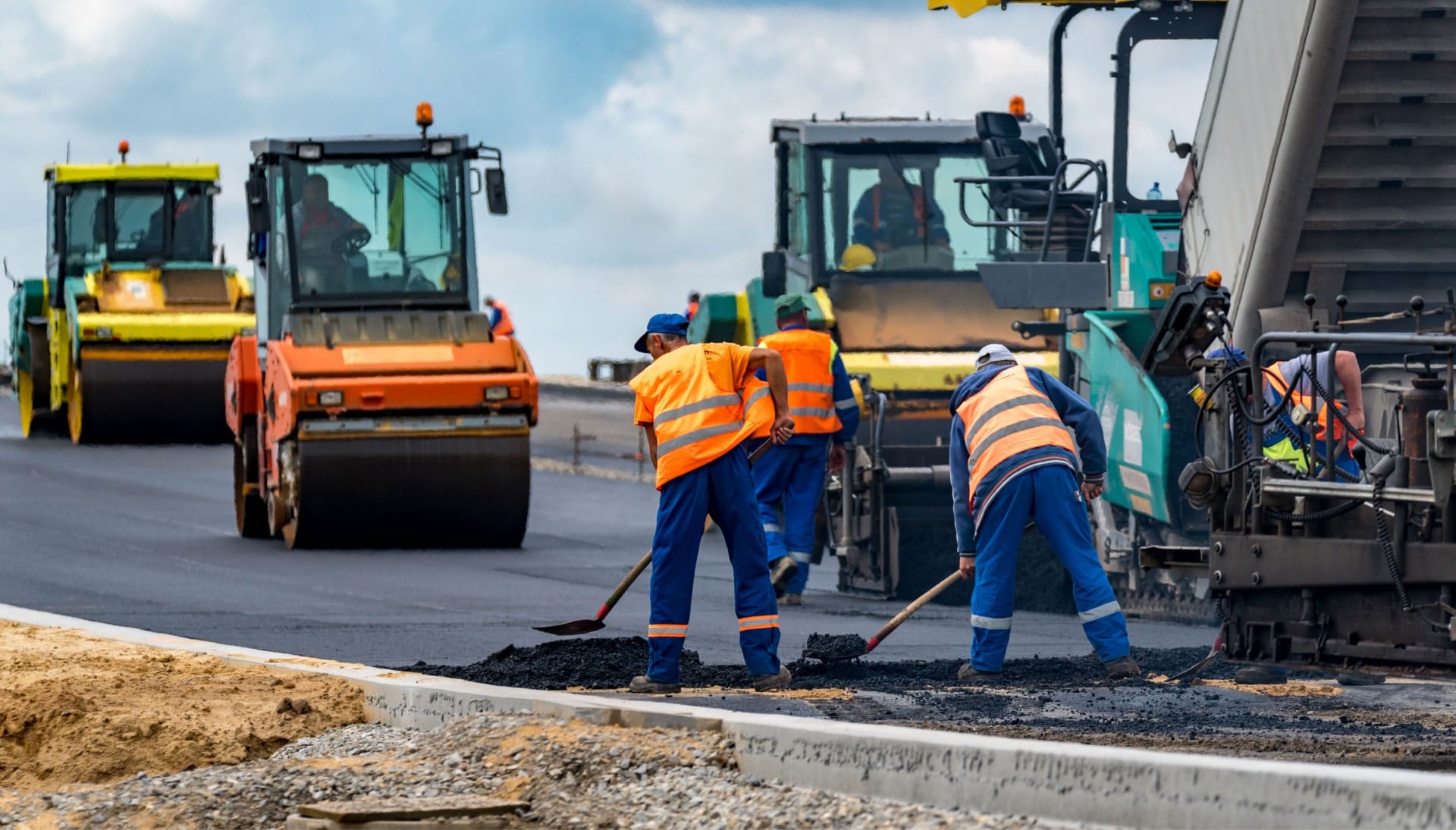 A group of construction workers wearing hard hats and reflective vests, operating heavy machinery and laying down asphalt on a newly excavated road in Rochester, showcasing the intricate process of building a sturdy and smooth surface.